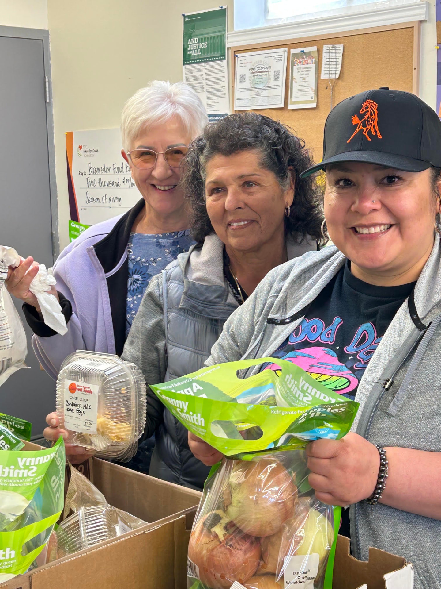 Three Brewster Food Pantry volunteers smiling behind boxes of fresh apples and produce