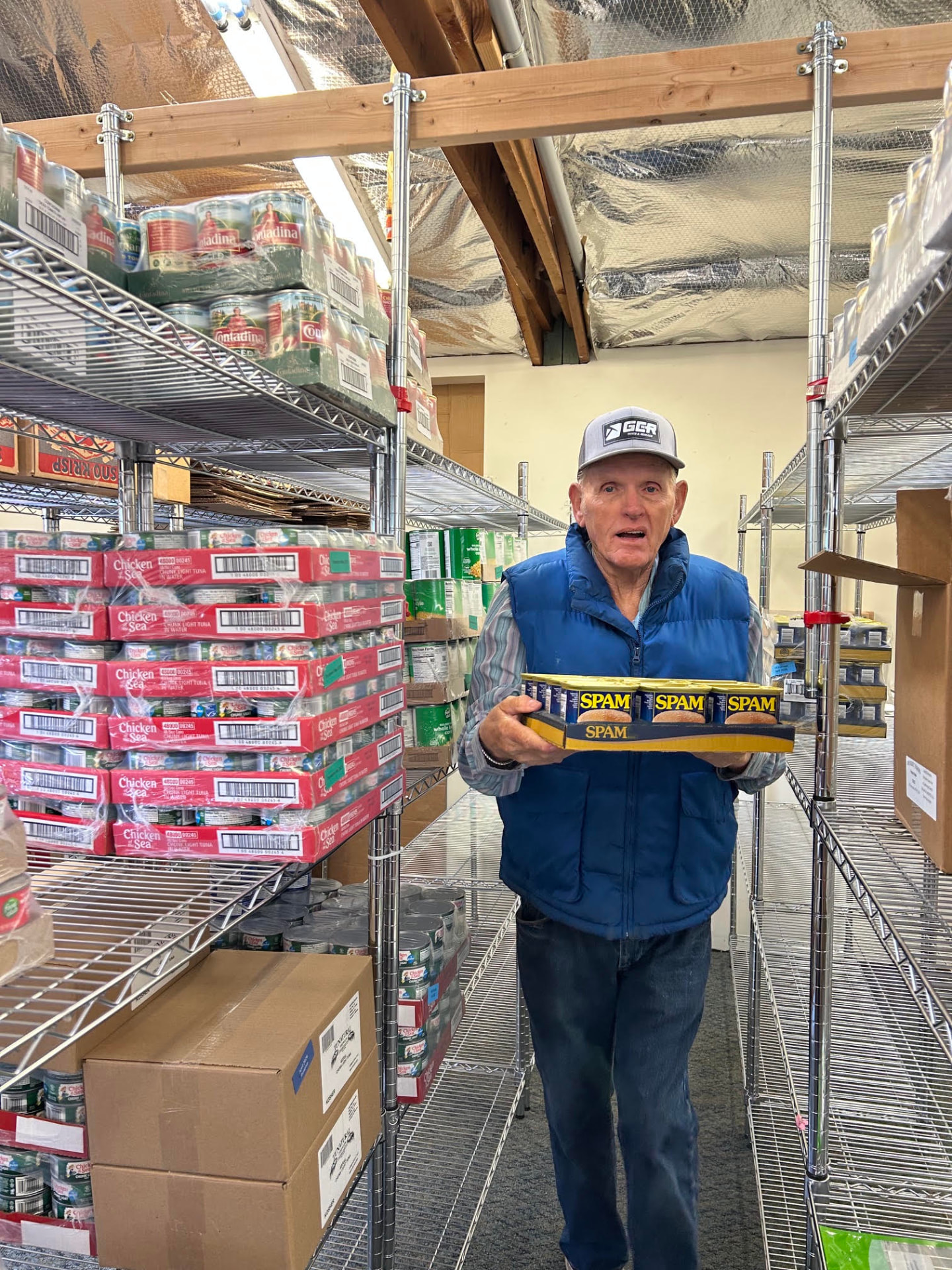 A volunteer carrying canned goods between fully stocked pantry shelves