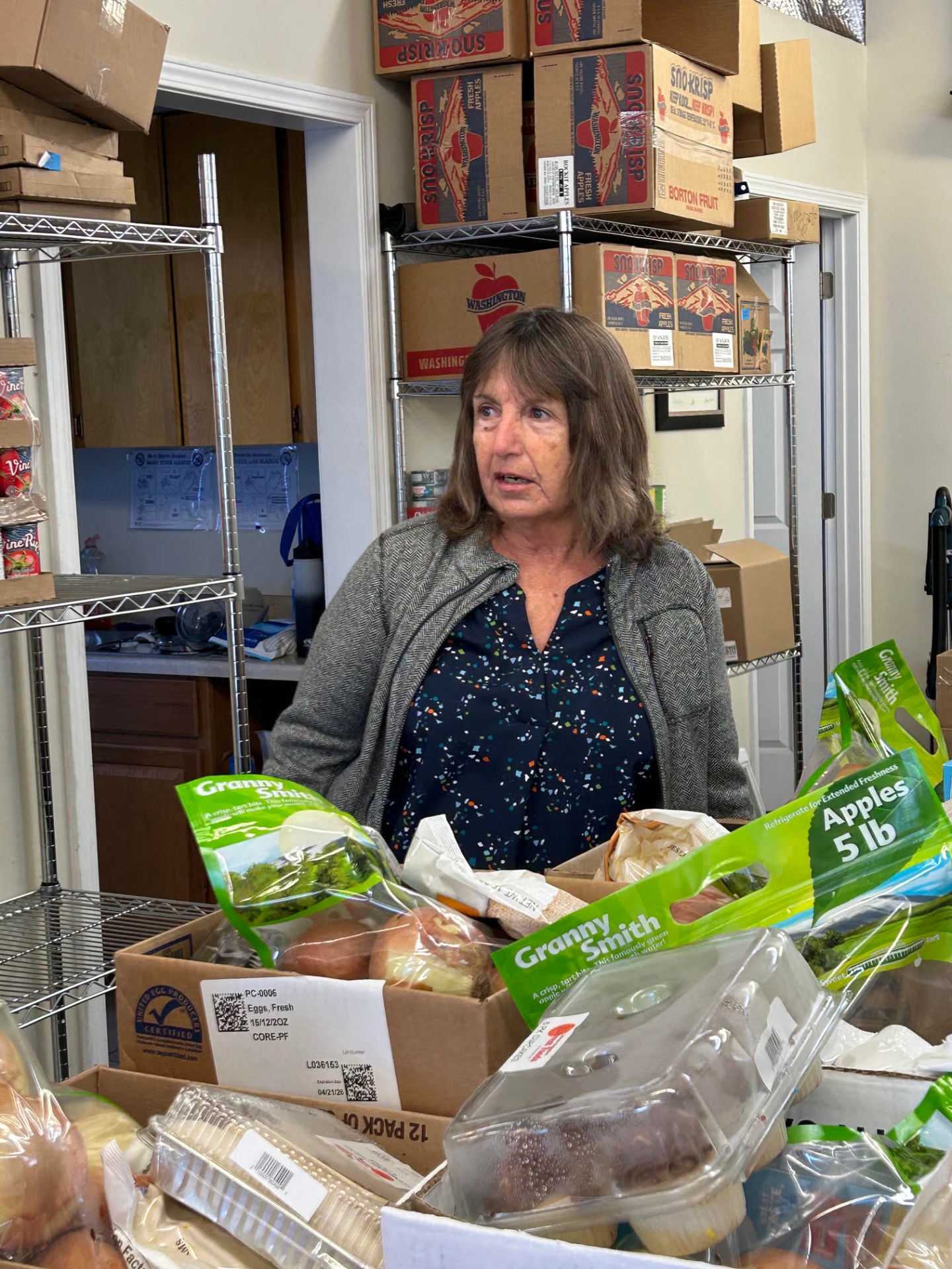 A pantry volunteer standing behind boxes of fresh produce inside the pantry